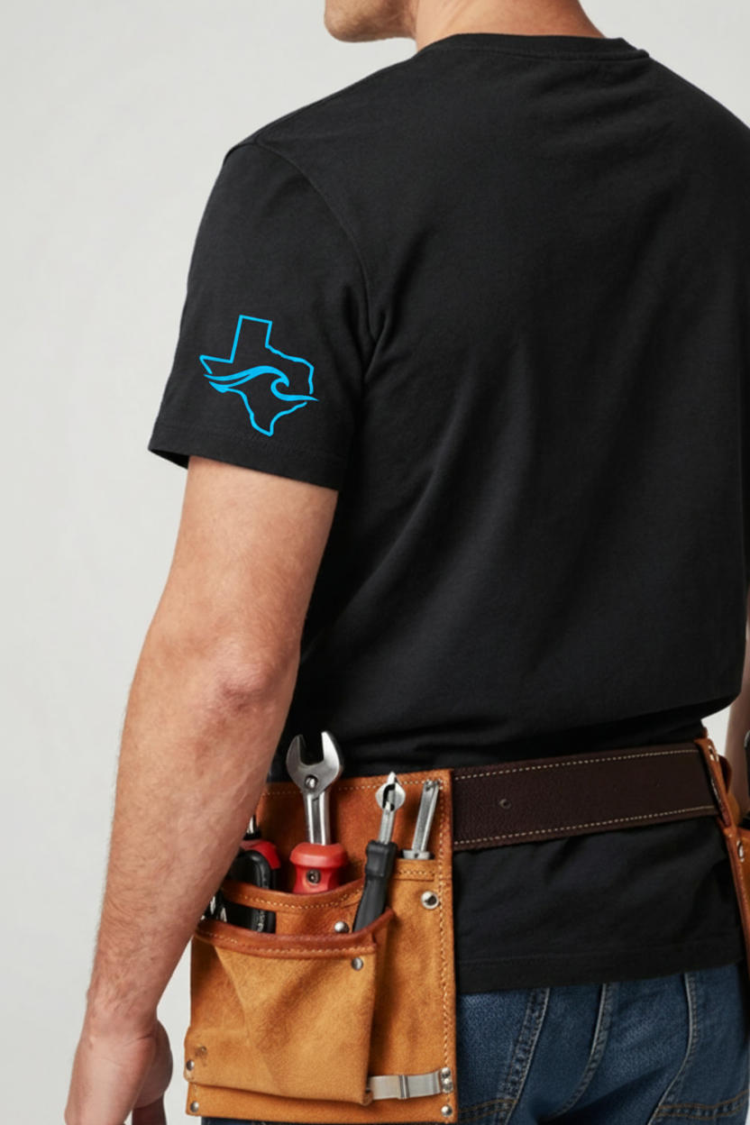 A man viewed from the back wearing a black short-sleeve t-shirt with a bright blue outline of Texas on the left sleeve, paired with a brown leather tool belt containing tools. The background is a clean, light gray studio backdrop.