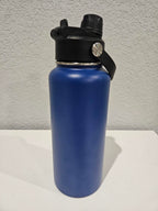 backside of a 32oz Blue hydro water bottle with black lid on a white surface against a gray wall