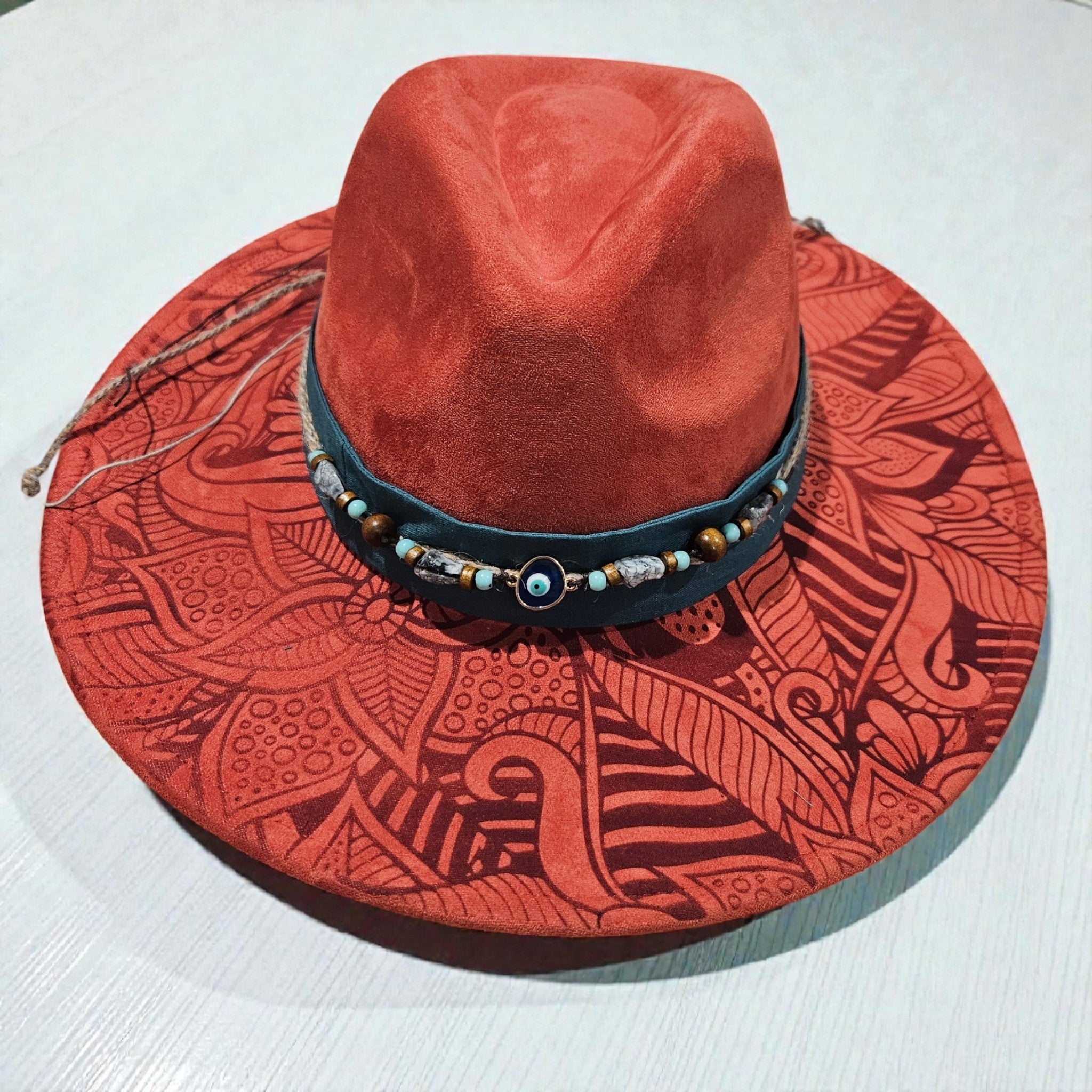 Rusty red wide brim hat featuring full laser engraved organic geometric pattern with teal fabric and blue beaded jute hat band